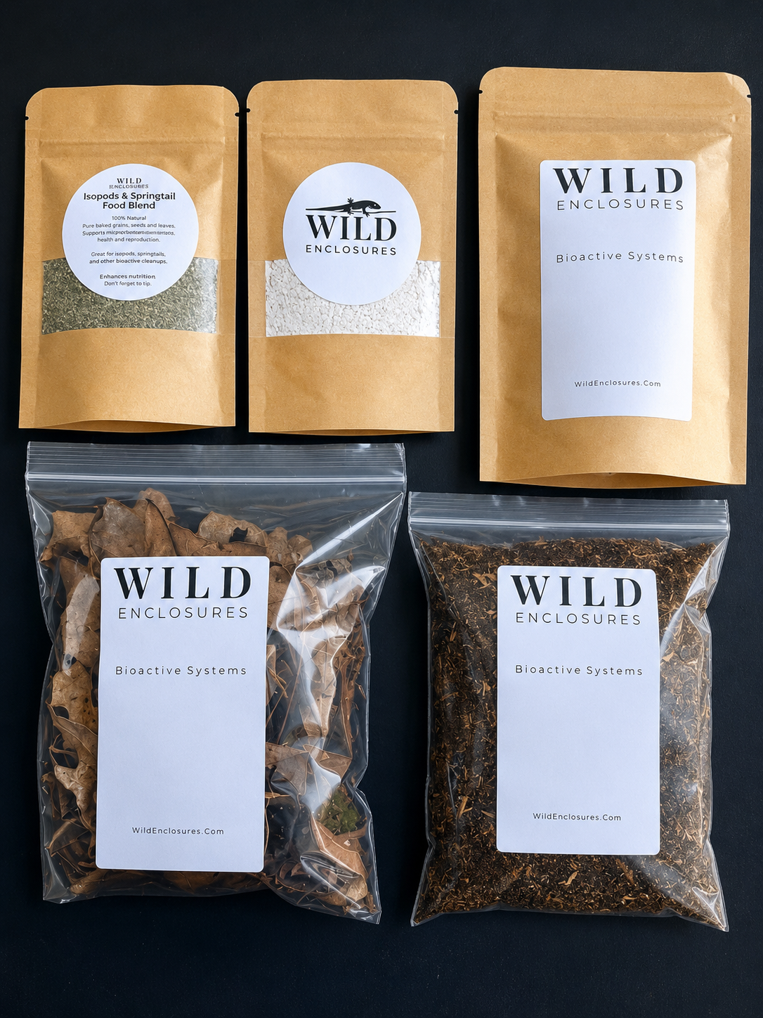 Flat lay of Wild Enclosures bioactive terrarium products arranged on a dark background, including isopod and springtail food blend, calcium supplement, bioactive substrate mix, dried leaf litter, and soil amendment, all packaged in branded kraft pouches and clear resealable bags.