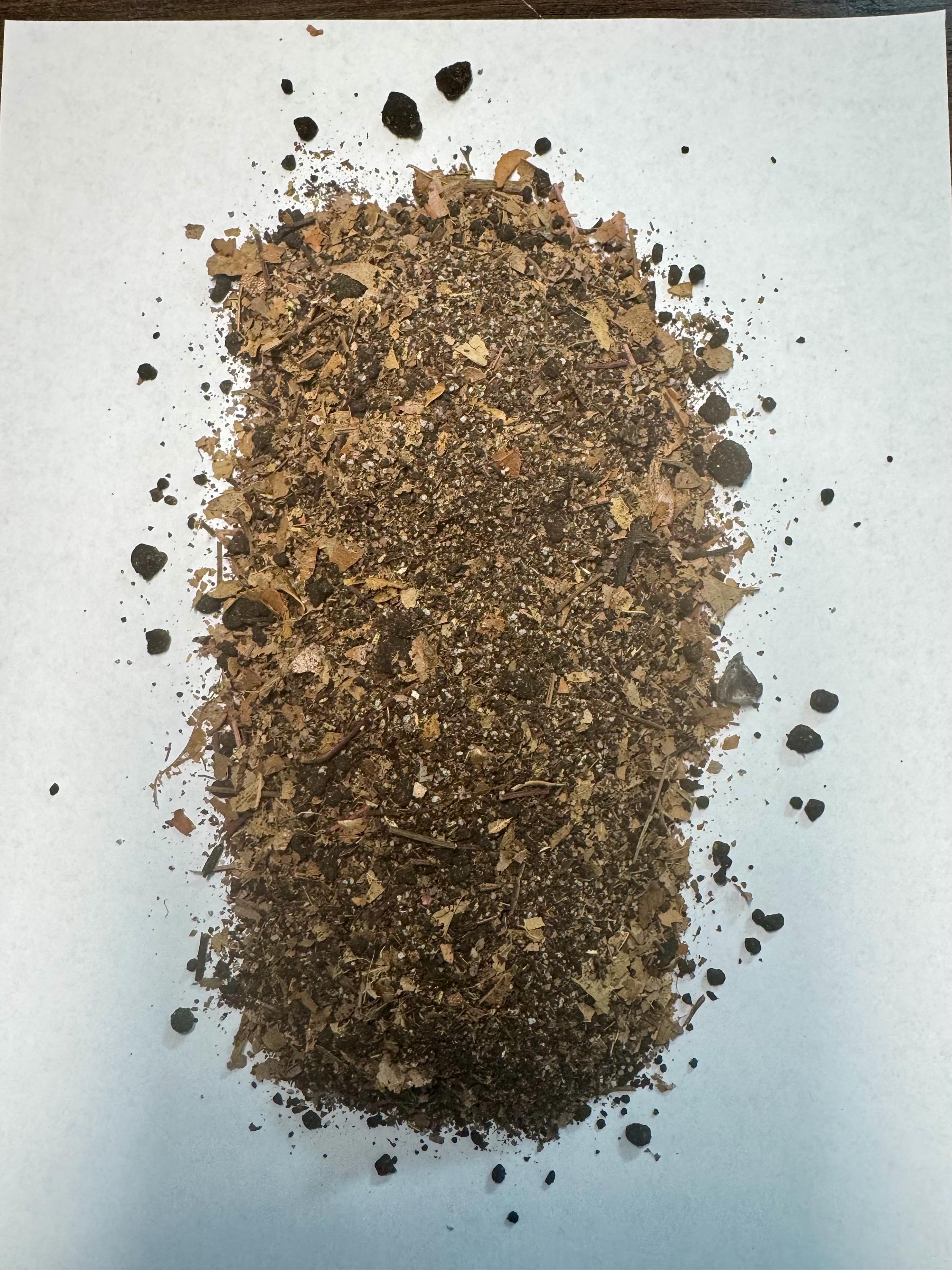 Close-up of SoilLife Booster bioactive substrate blend with leaf litter, wood fragments, and organic soil particles on white background